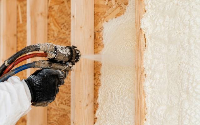 Close view of a spray foam gun applying foam to a wall